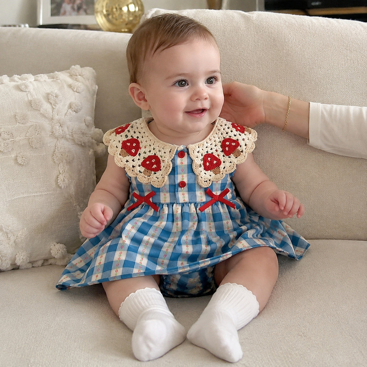 Baby blue gingham romper dress with crochet strawberry collar and red bows - worn indoor lifestyle view