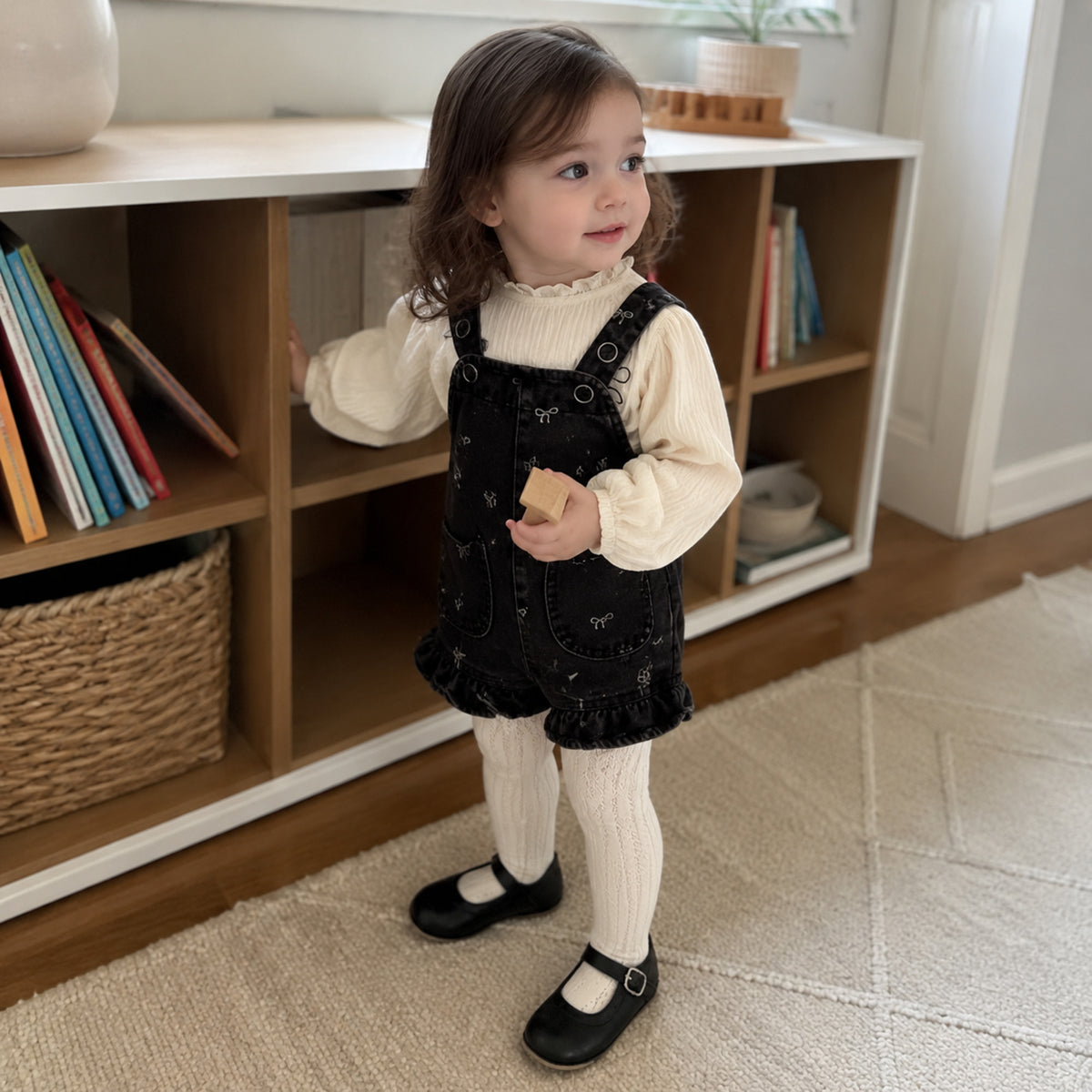Toddler wearing the ivory blouse with black bow denim romper and cream tights