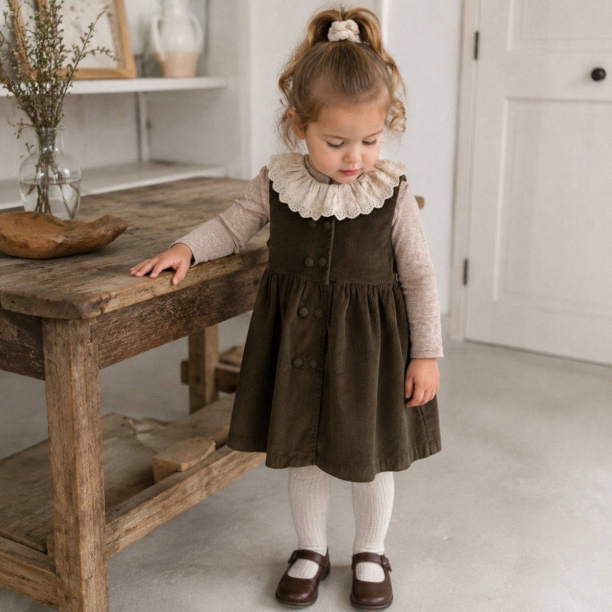 Toddler wearing the eyelet collar top with olive corduroy pinafore and cream tights