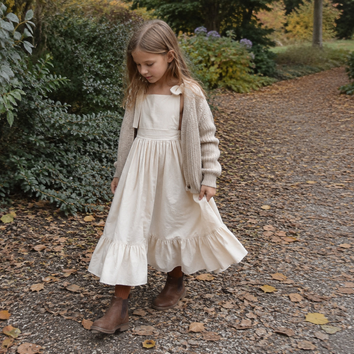 Older girl wearing ivory tie-shoulder maxi dress with cardigan on an autumn path