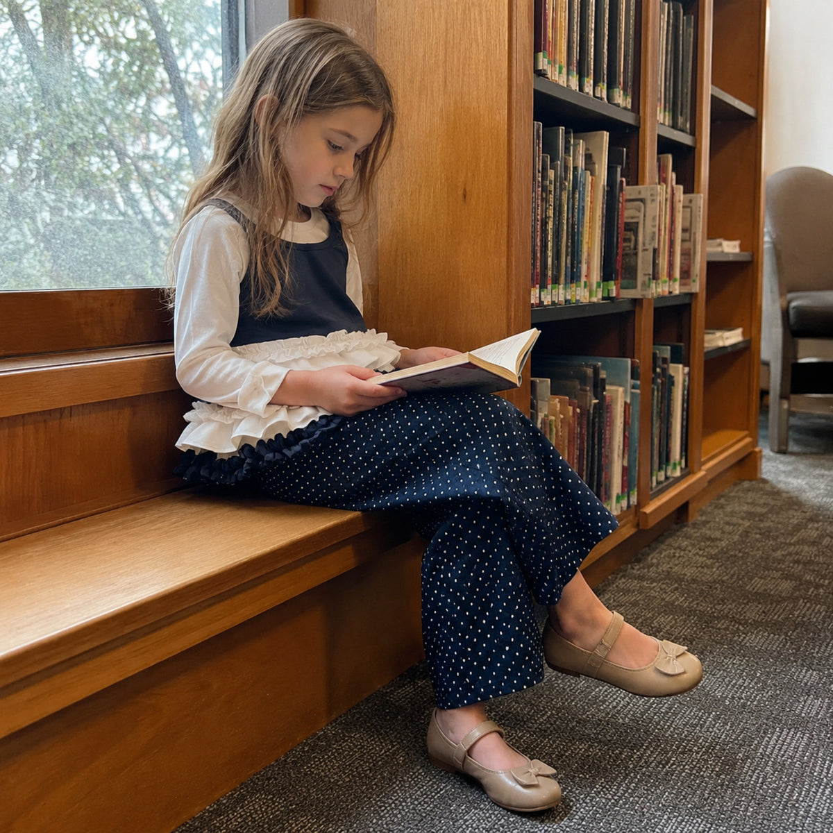 Older girl reading in navy polka dot pants and layered ruffle top