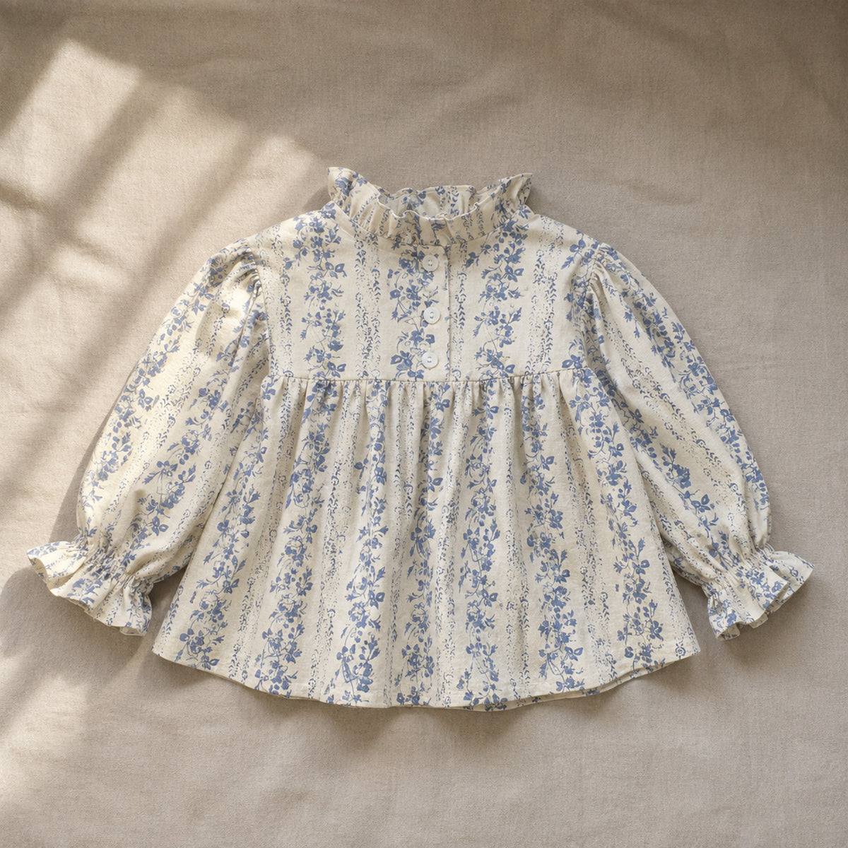 Ivory and blue botanical ruffle-collar girls blouse laid on natural linen