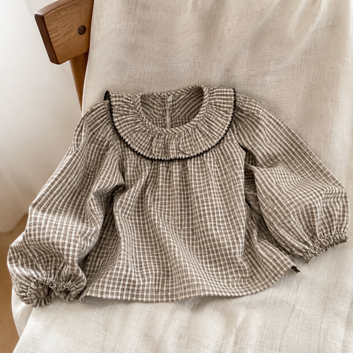 Brown micro-gingham long-sleeve ruffle collar blouse displayed on a linen chair