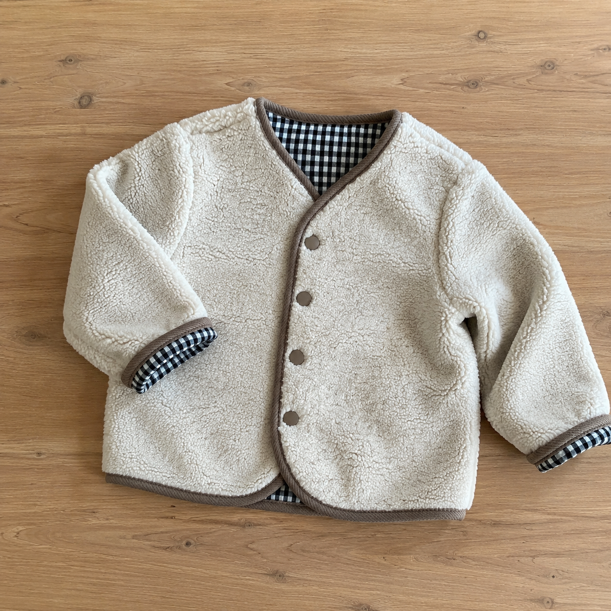 Ivory sherpa side of the reversible toddler jacket on a natural wooden table