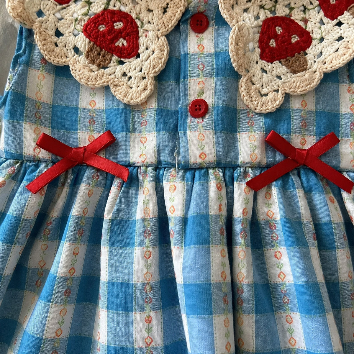 Baby blue gingham romper dress with crochet strawberry collar and red bows - fabric and trim close-up