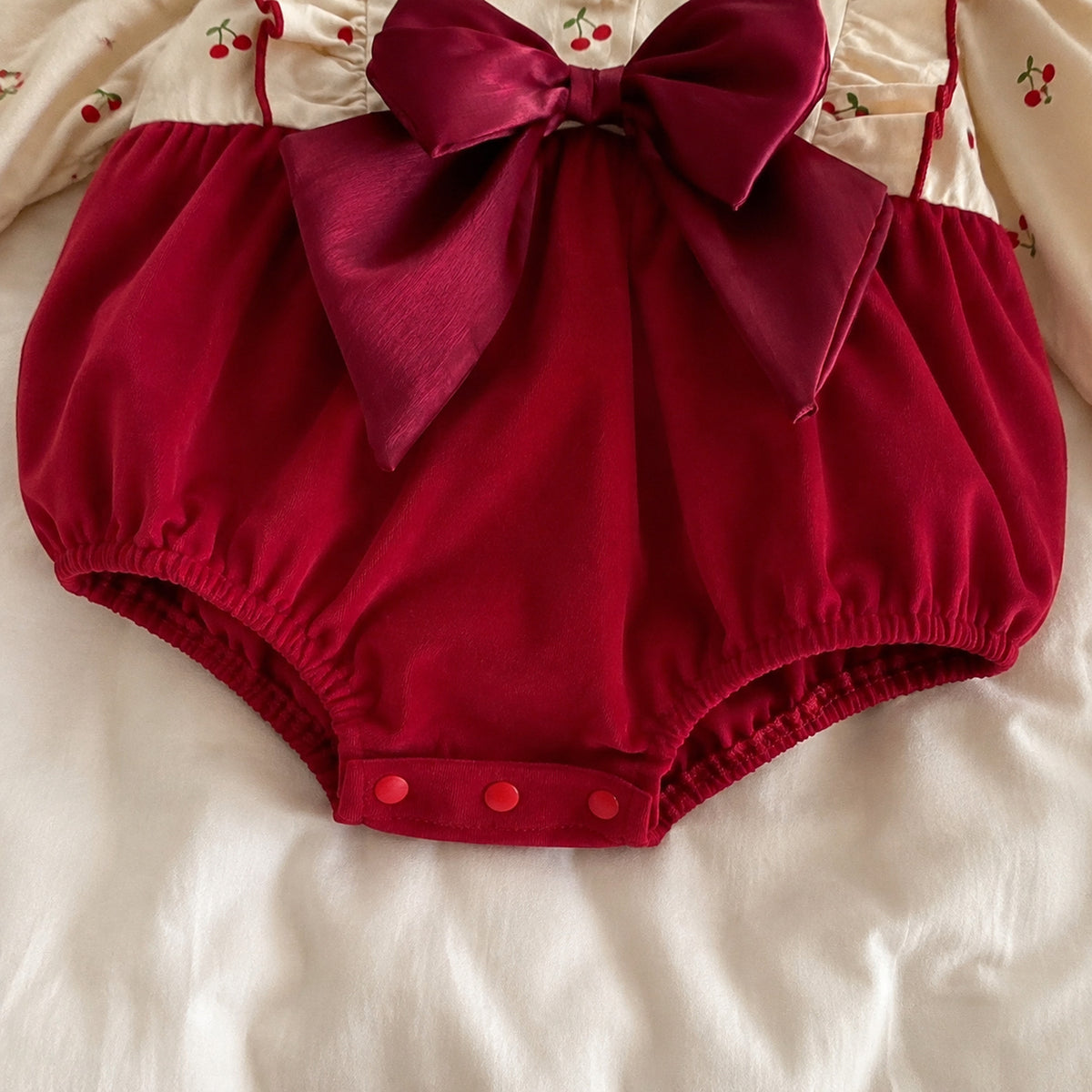Baby burgundy velvet romper with cherry print long sleeves and large bow - construction and closure detail