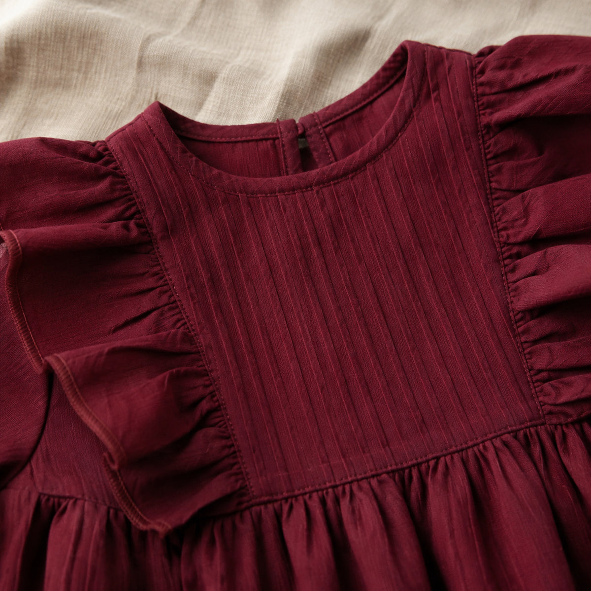 Close-up of wine red pintuck bib, round neckline and shoulder ruffles