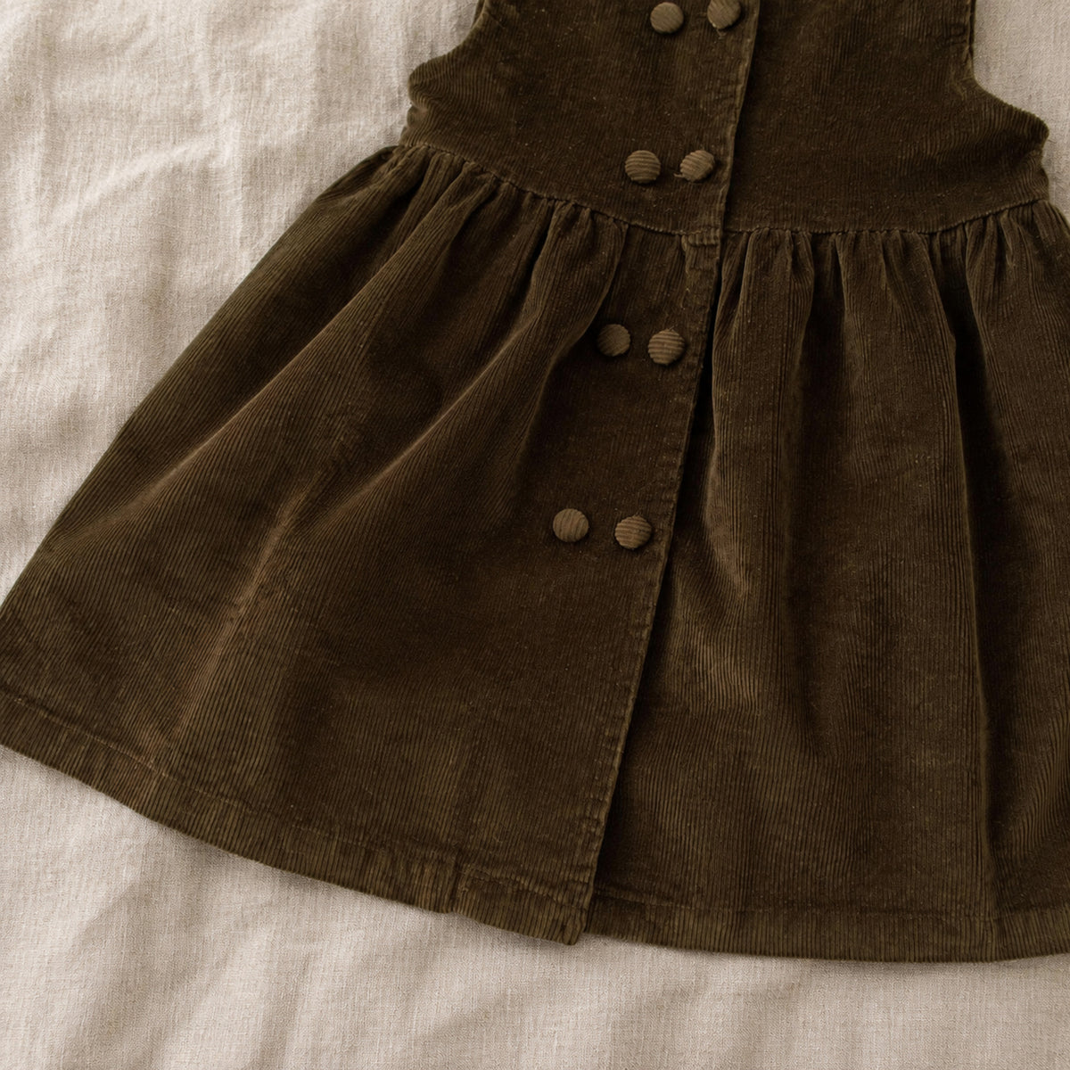 Close-up of the olive corduroy pinafore gathered skirt, buttons and hem