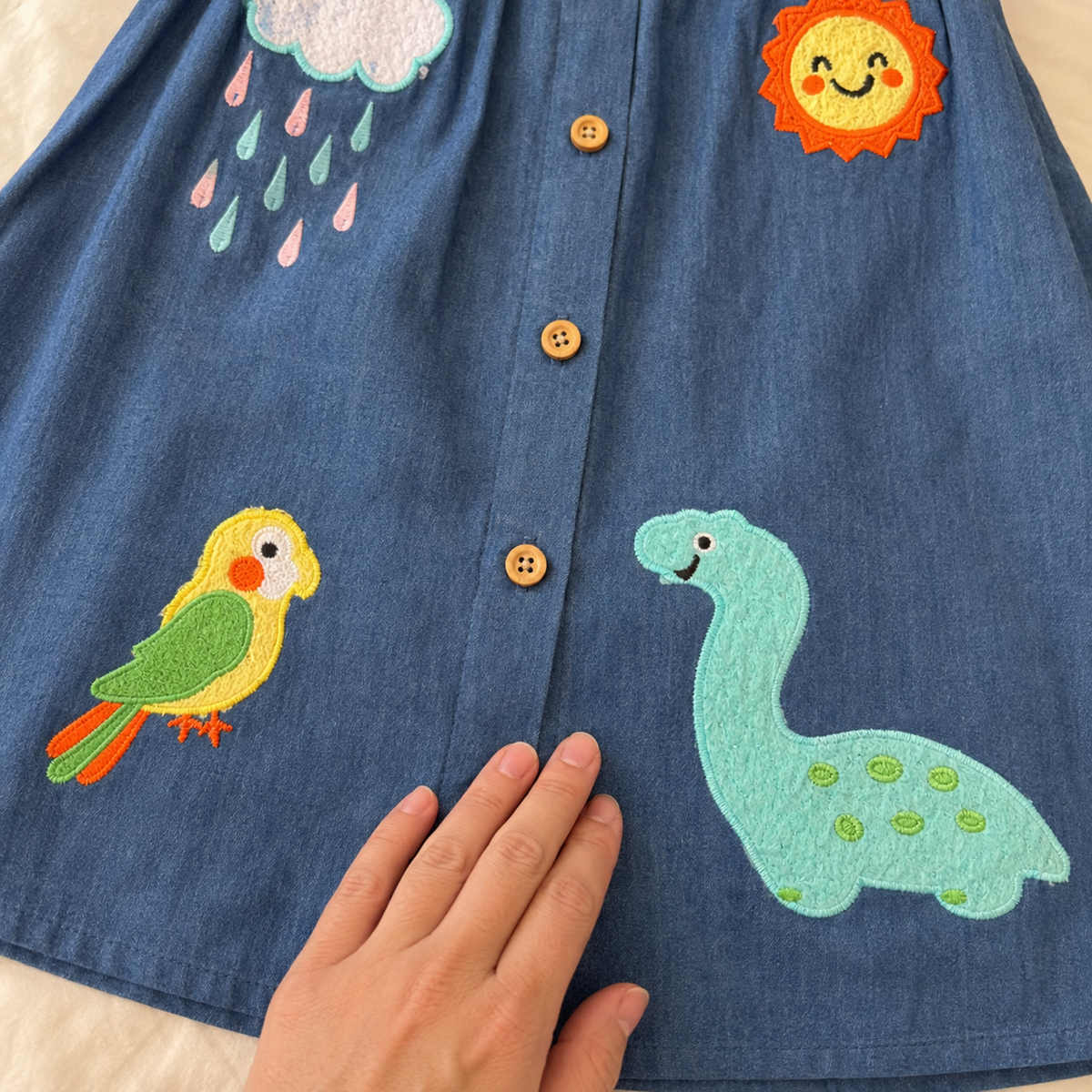 Close-up of parrot and dinosaur appliqués on denim