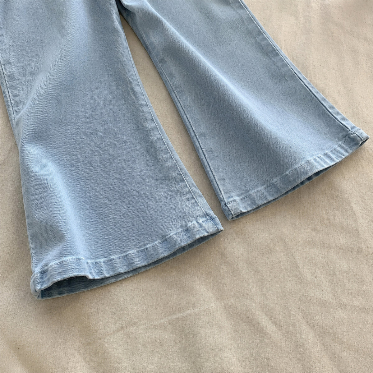 Close-up of the gently flared denim pant legs and stitched hems