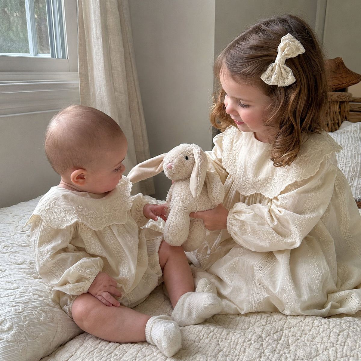 Baby and older sister wearing matching ivory outfits at home