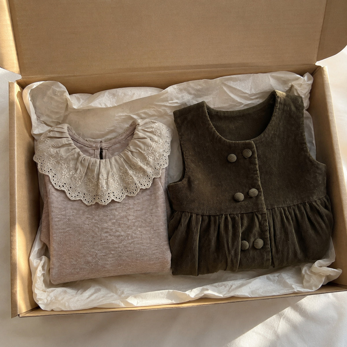 Oatmeal eyelet top and olive corduroy pinafore folded separately in a kraft box
