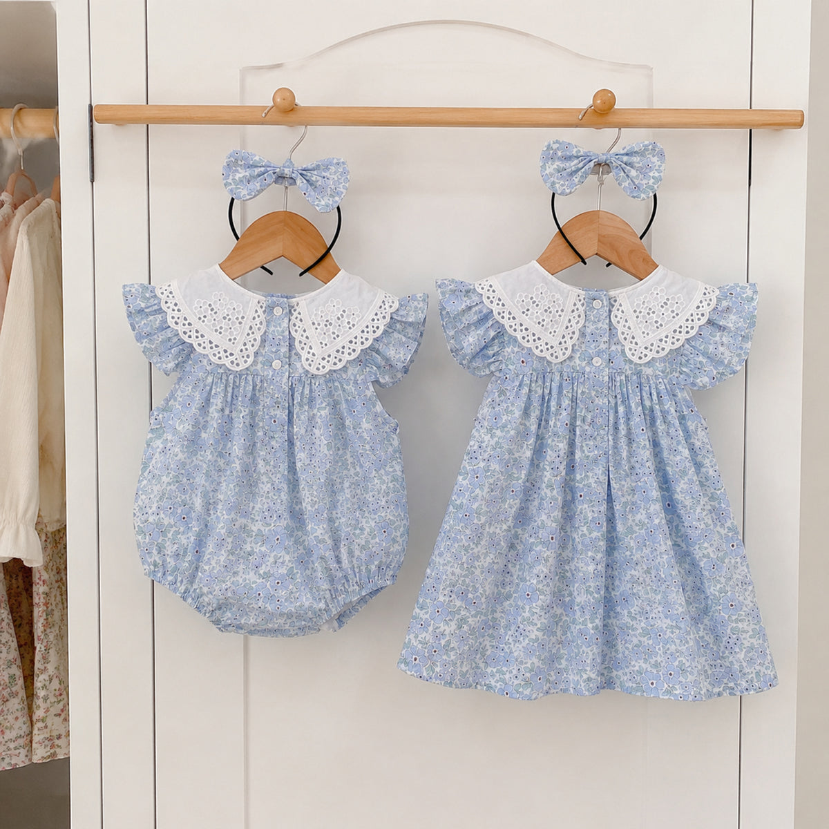 Back view of blue floral romper and dress on wooden hangers