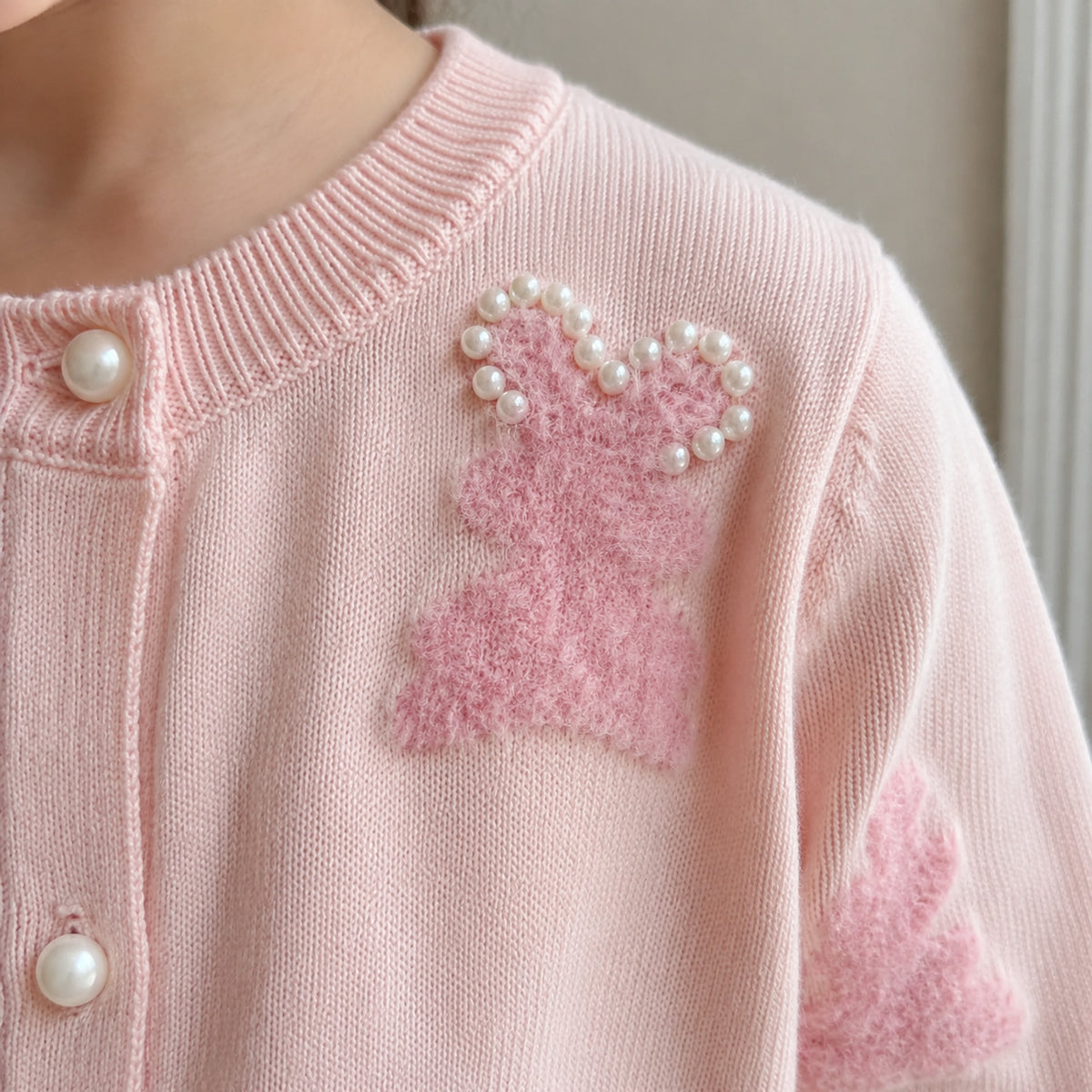 Close-up of fuzzy bunny motif and pearl bead detail on pink cardigan