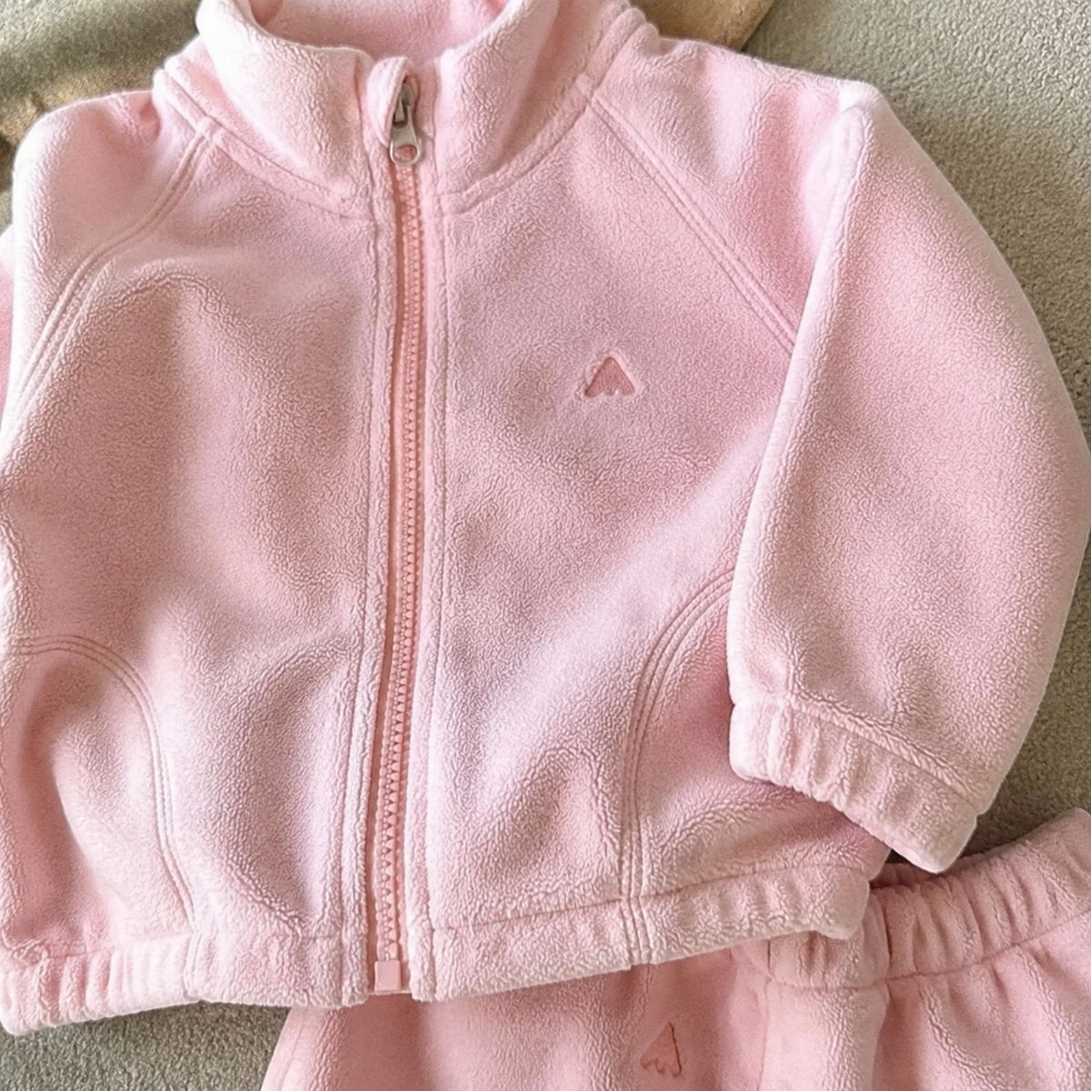 Close-up of light pink fleece zipper, collar, cuff and chest emblem