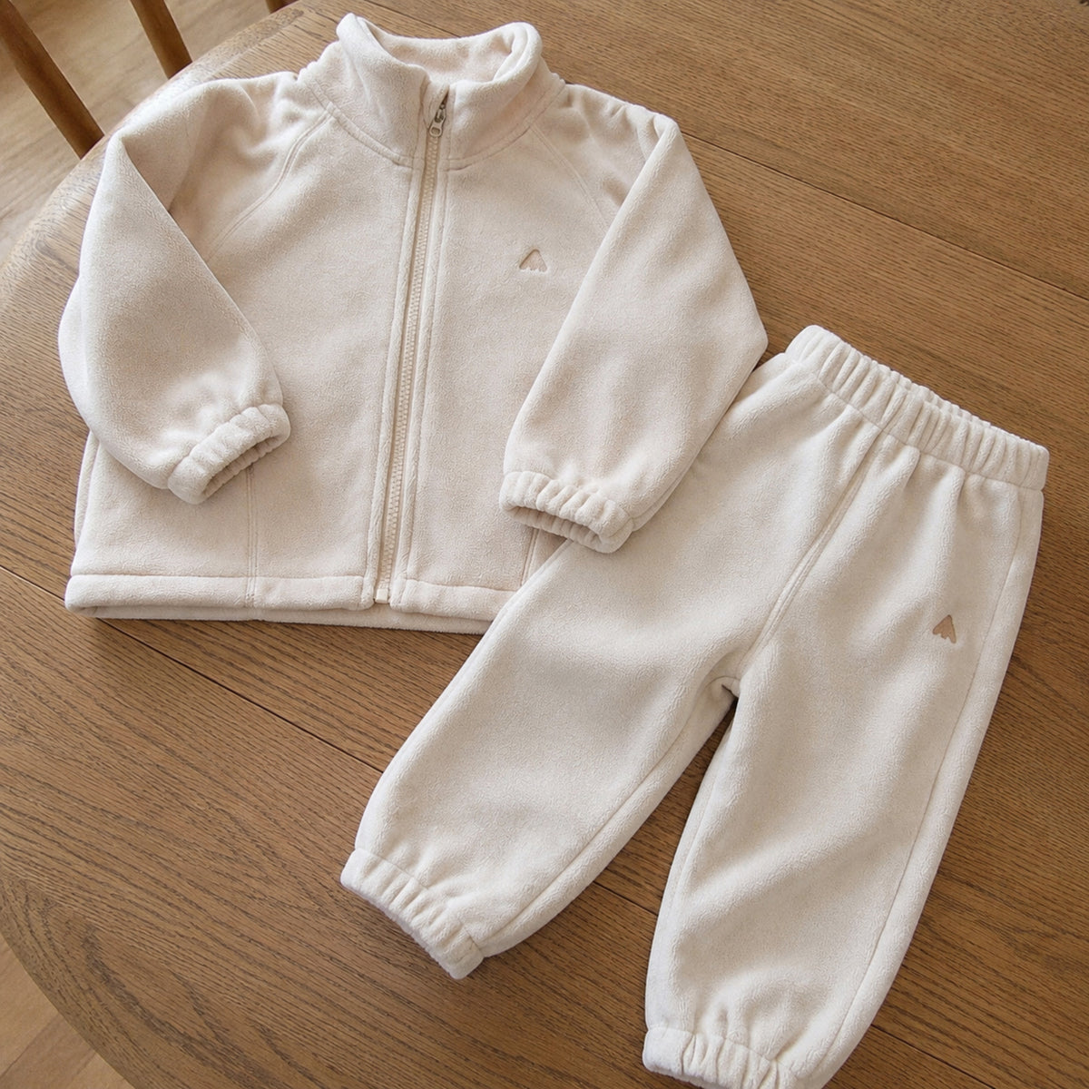 Beige fleece zip jacket and joggers laid separately on an oak table