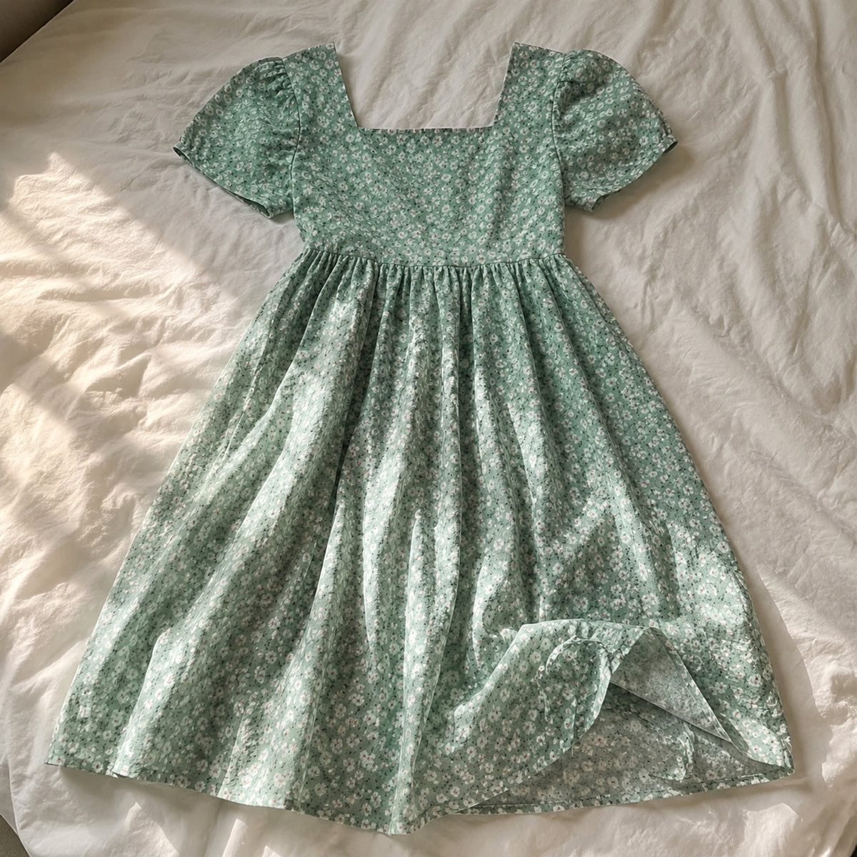 Sage green floral girls dress laid naturally on a bed