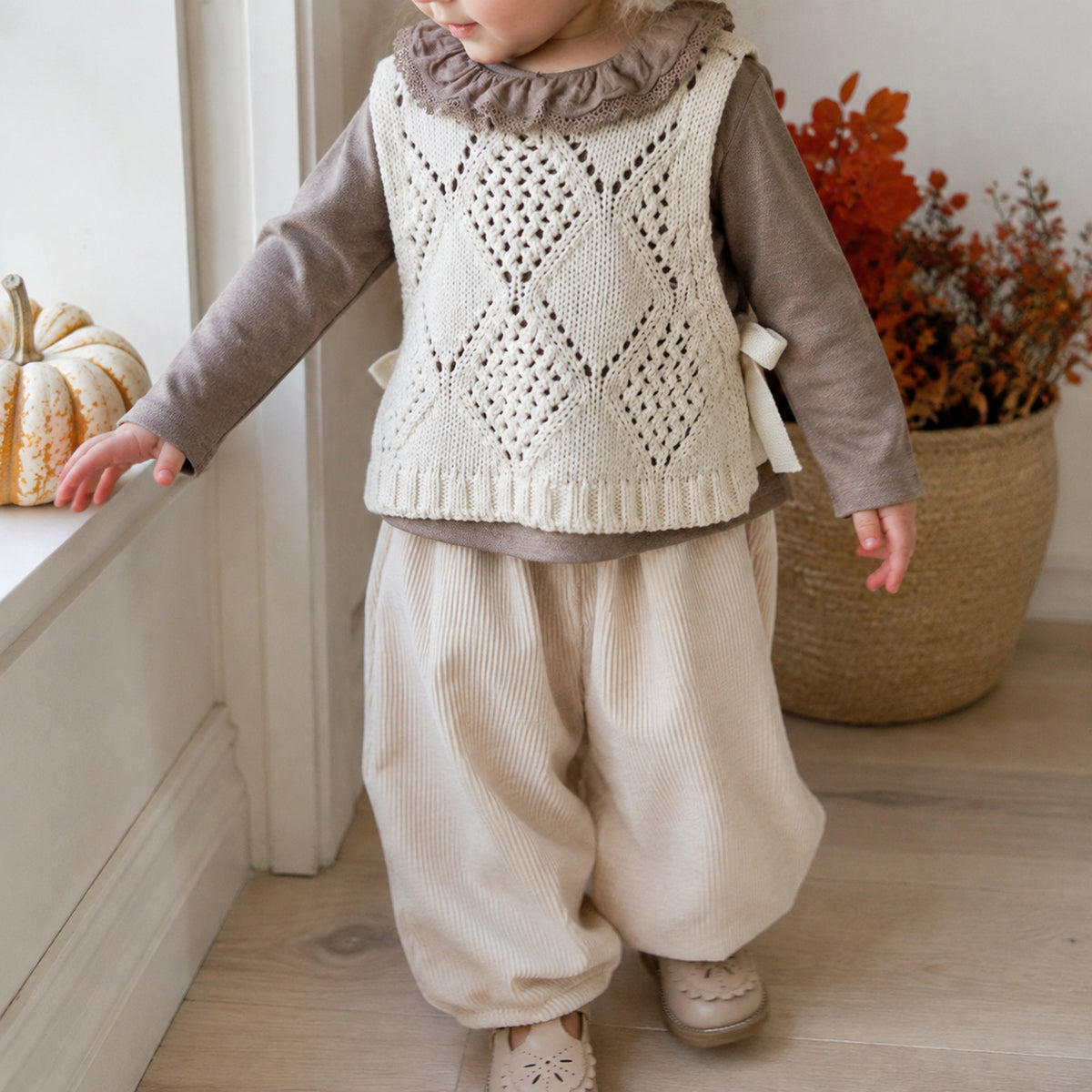 American toddler wearing the neutral cream knit vest, taupe ruffle top and corduroy pants fall outfit