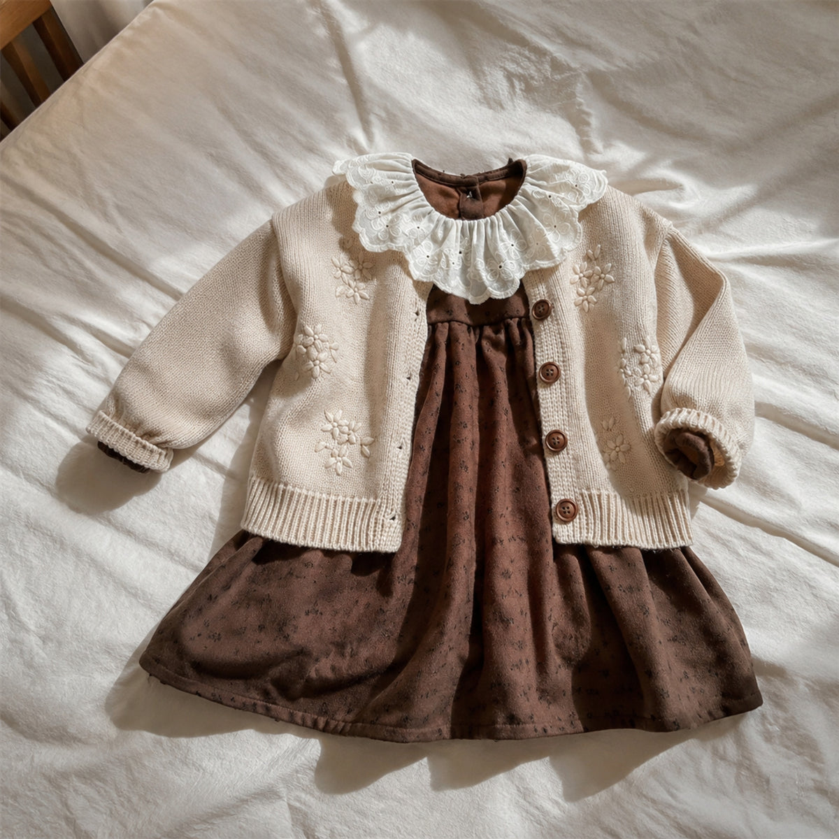 Cream cardigan and brown eyelet-collar dress set laid naturally on a bed
