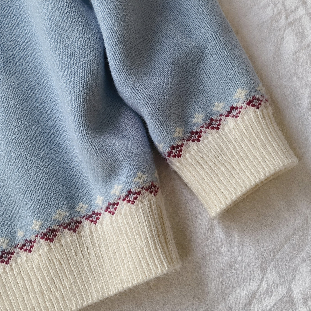 Blue cardigan cream ribbed cuff and burgundy knit trim close-up