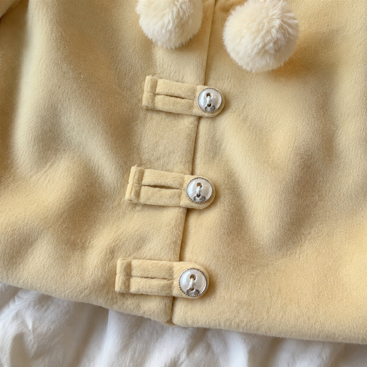 Close-up of three pearl-style toggle closures on the pale yellow jacket