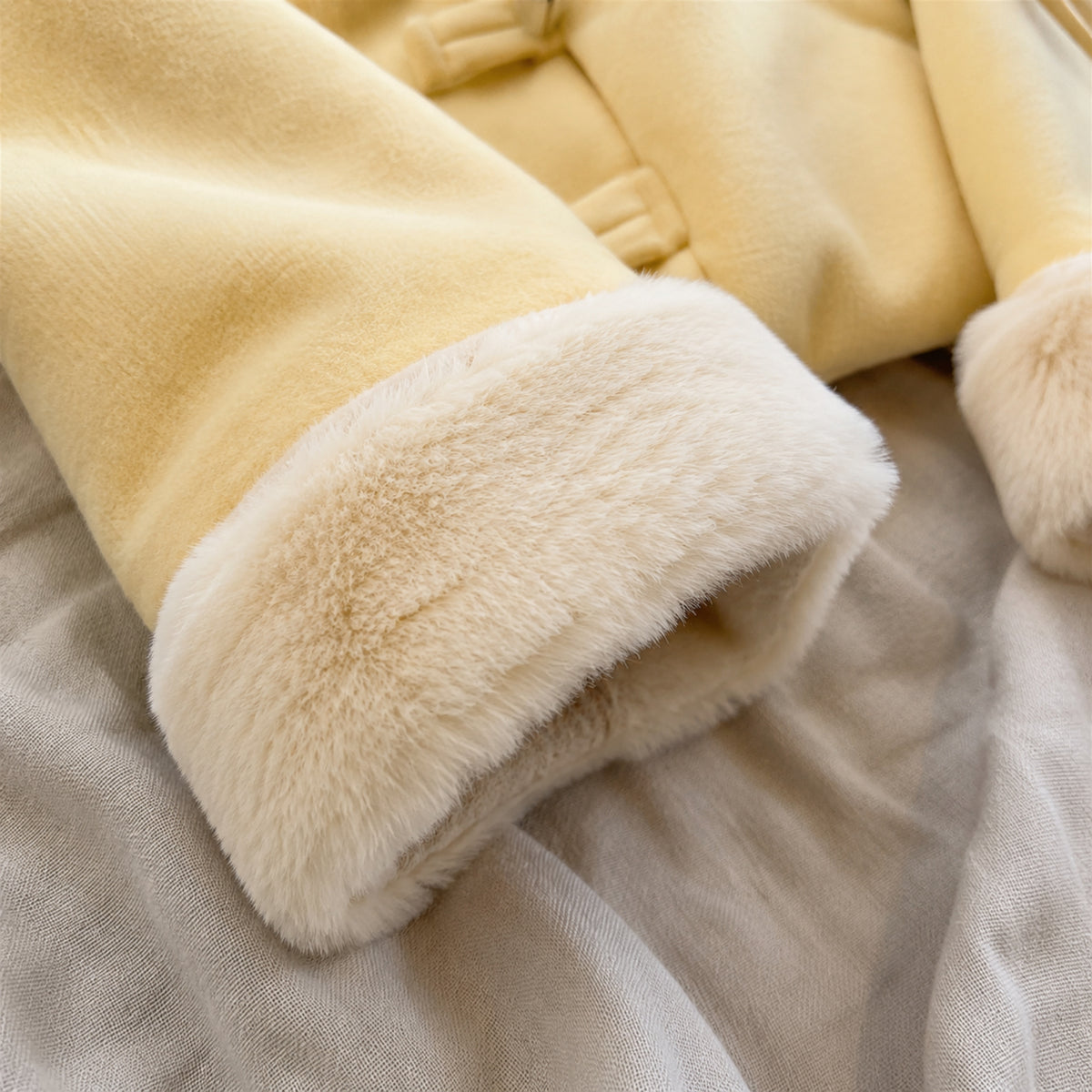 Close-up of the plush cream faux fur cuff and soft yellow jacket fabric