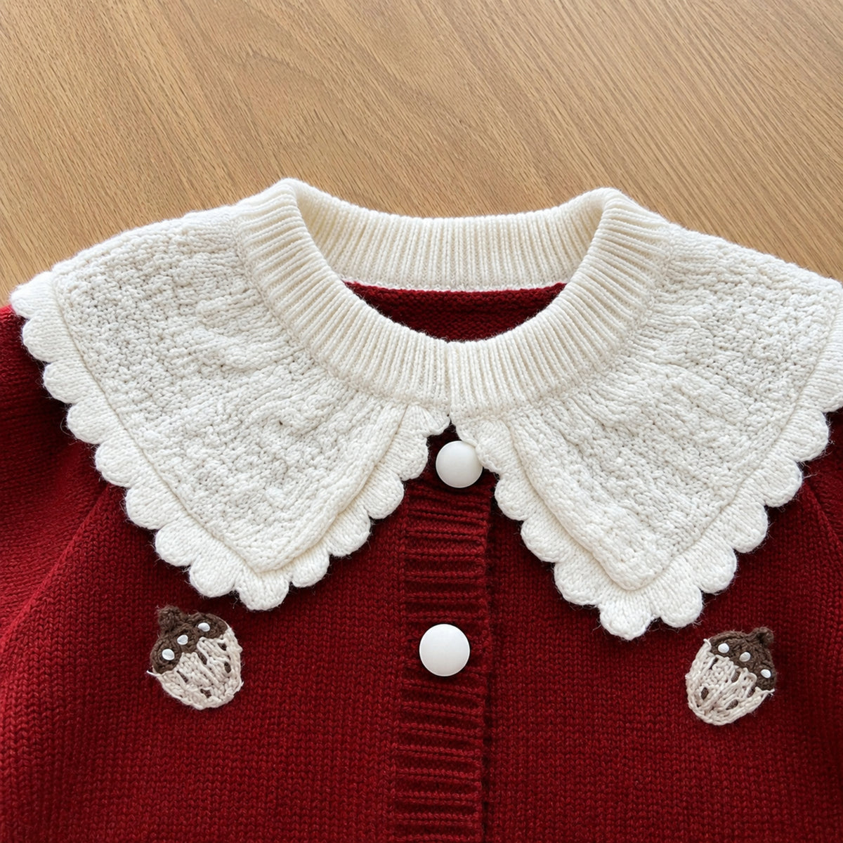 Close-up of burgundy knit cardigan, ivory scalloped collar and pale strawberry appliques