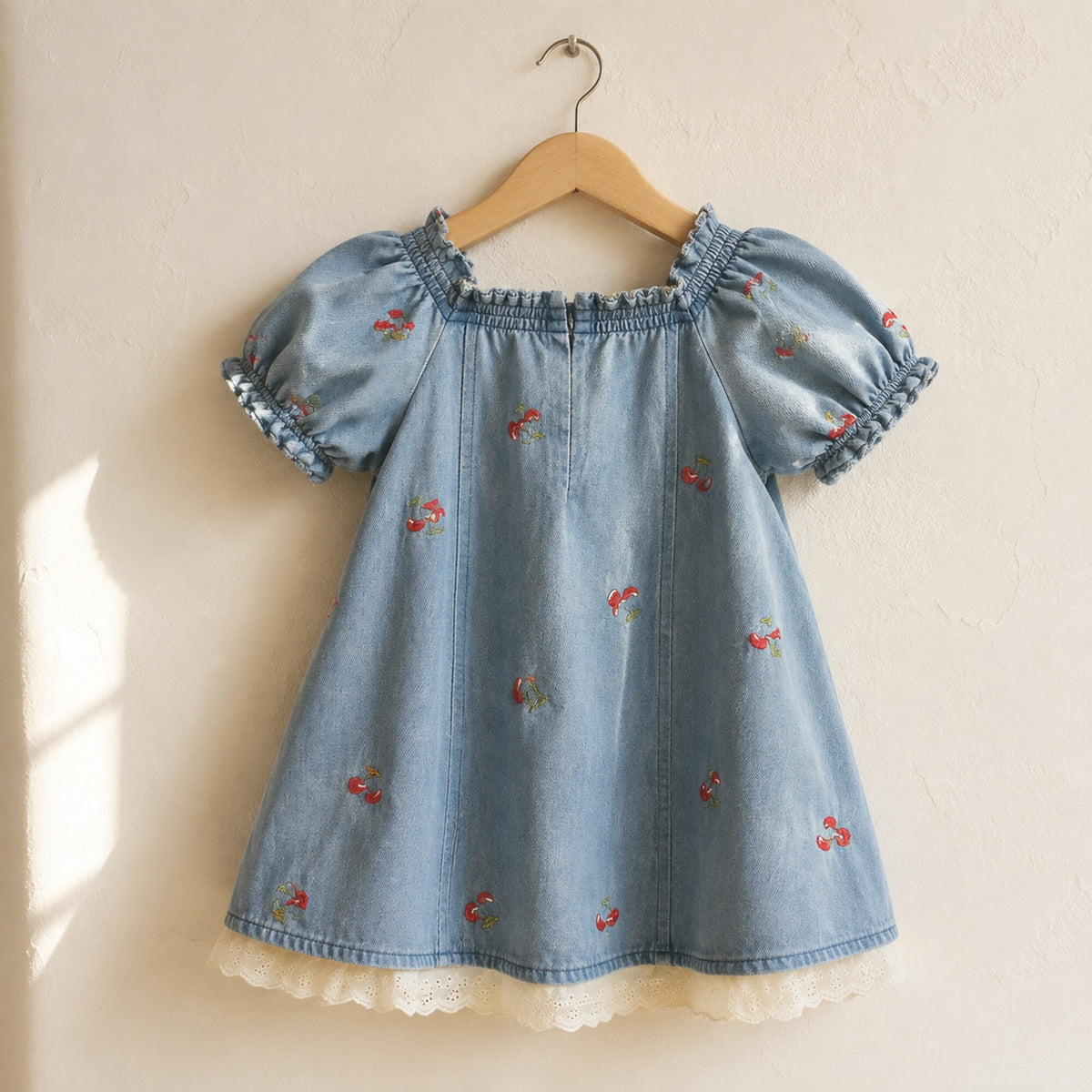 Back view of the cherry embroidered denim girls dress on a wooden hanger