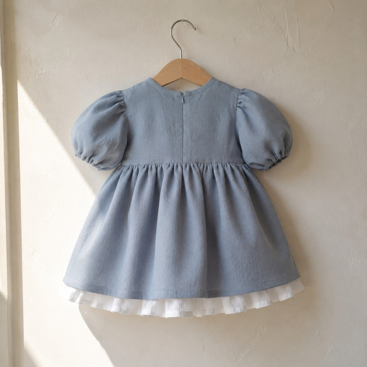 Back view of the dusty blue linen girls dress on a wooden hanger