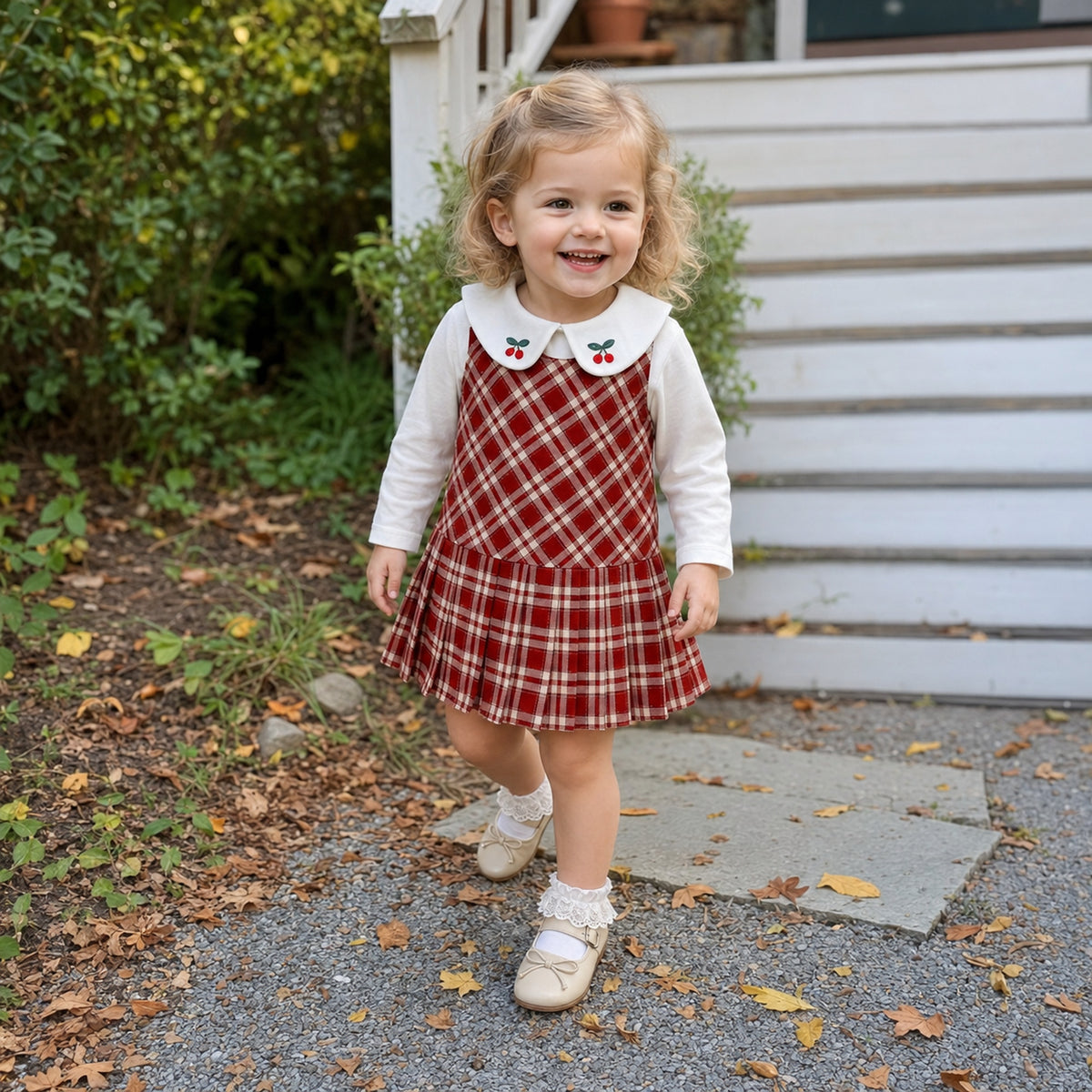 Toddler girl wearing a red plaid jumper dress outdoors in autumn