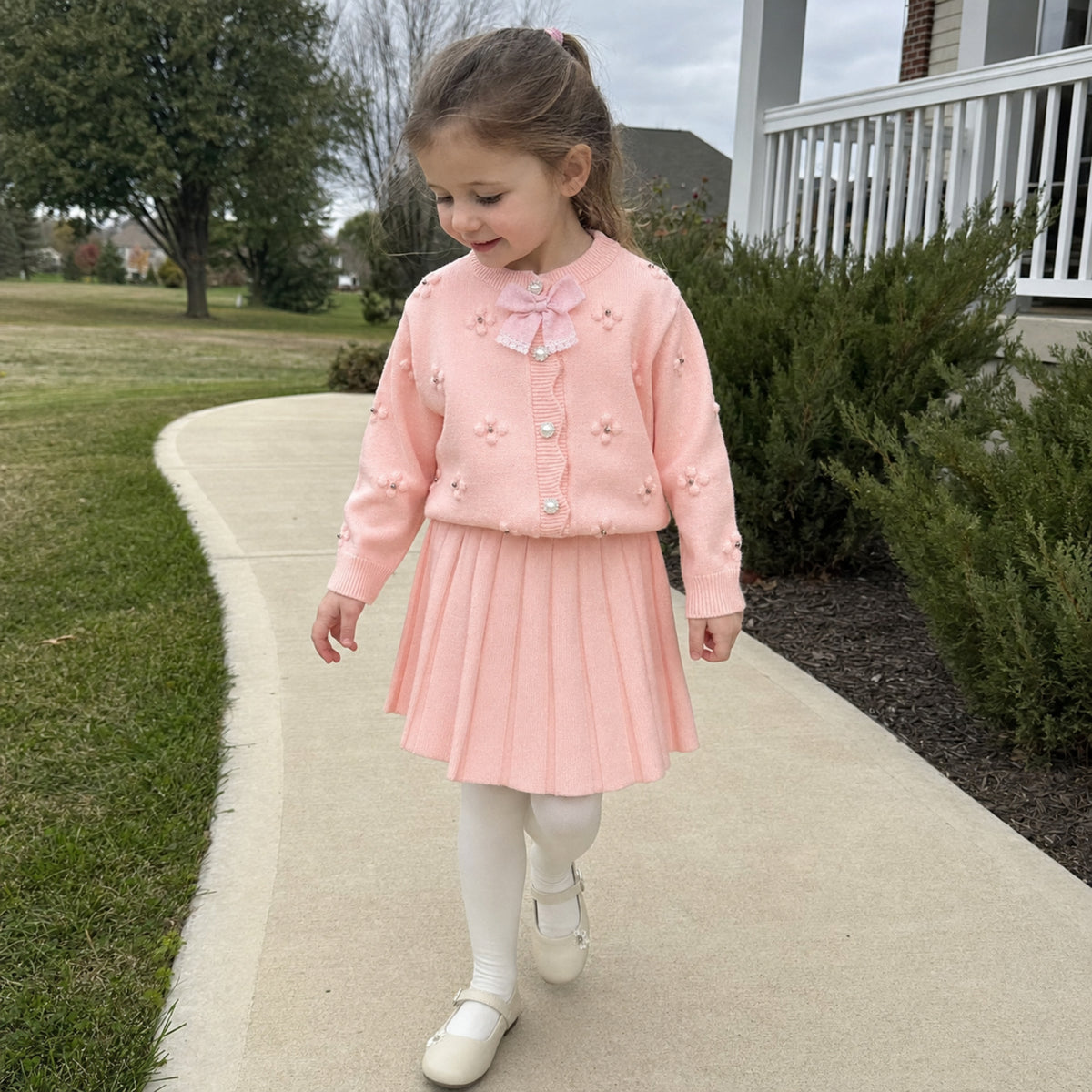Girl wearing pink bow cardigan skirt set outdoors