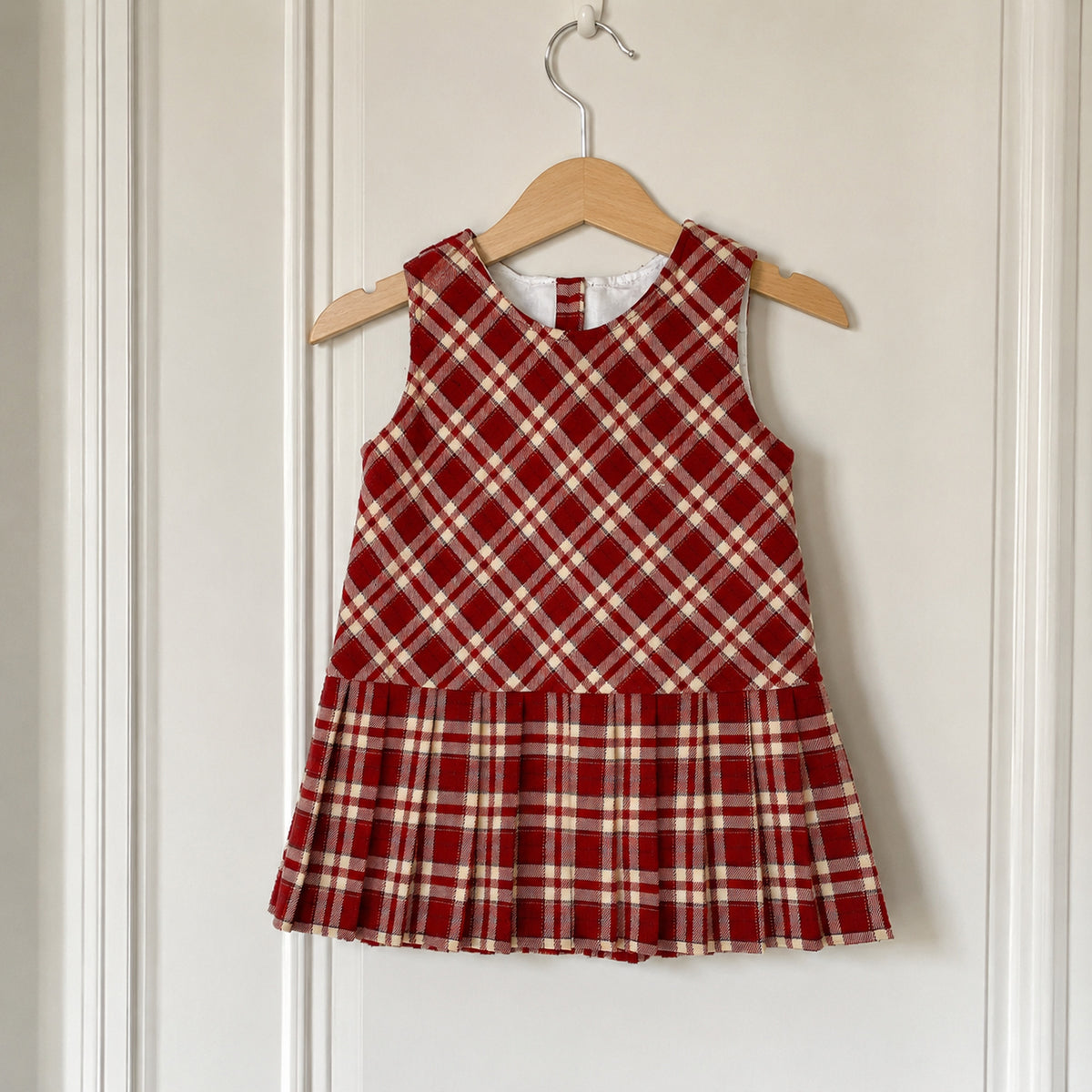 Red plaid A-line jumper dress hanging on a wooden hanger