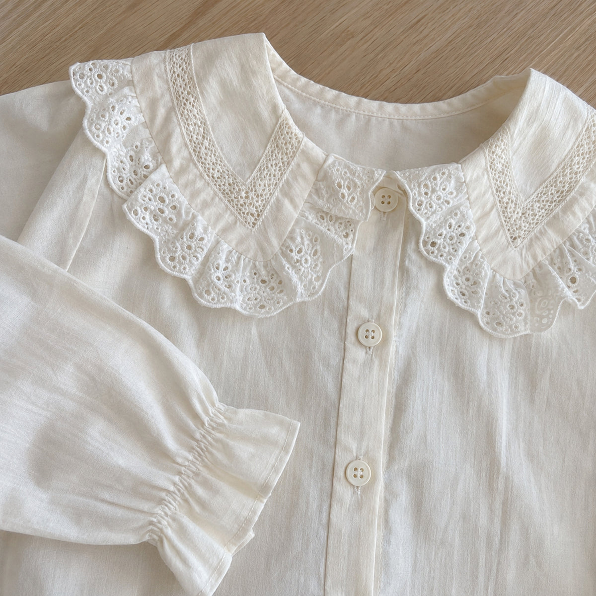 Close-up of the ivory eyelet lace collar, buttons and ruffled cuff