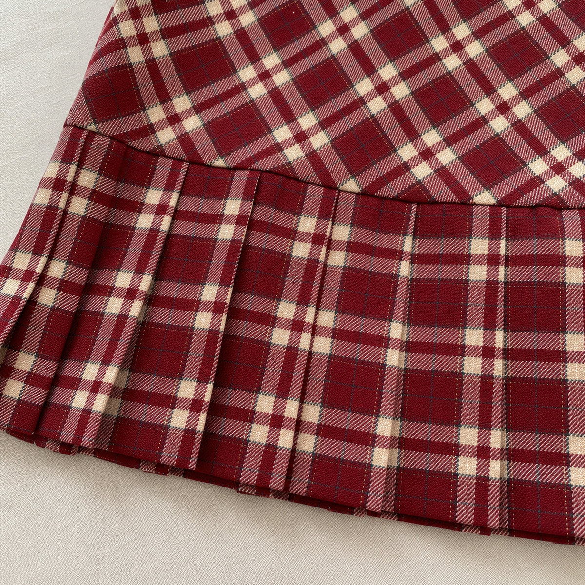 Close-up of red and cream plaid fabric, waist seam and pleated skirt