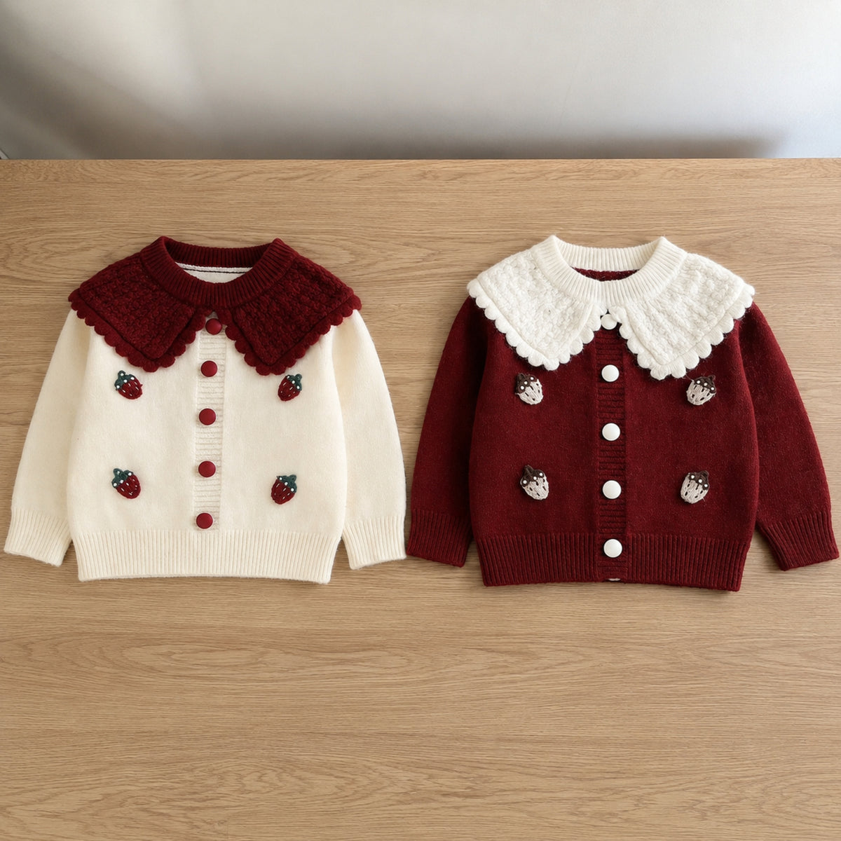 Ivory and burgundy strawberry knit cardigans only on a plain table