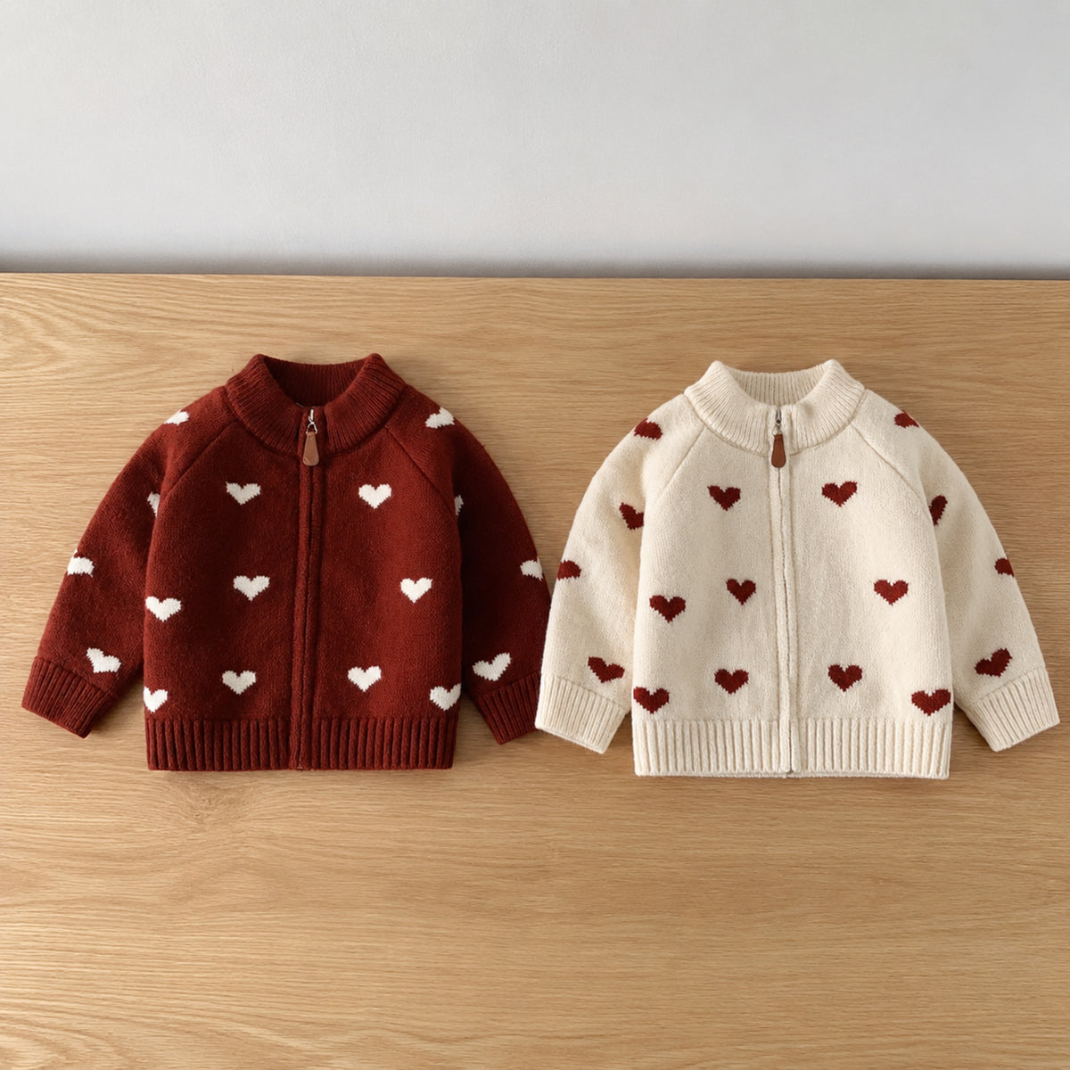 Red and off-white girls heart knit zip cardigans on a plain table